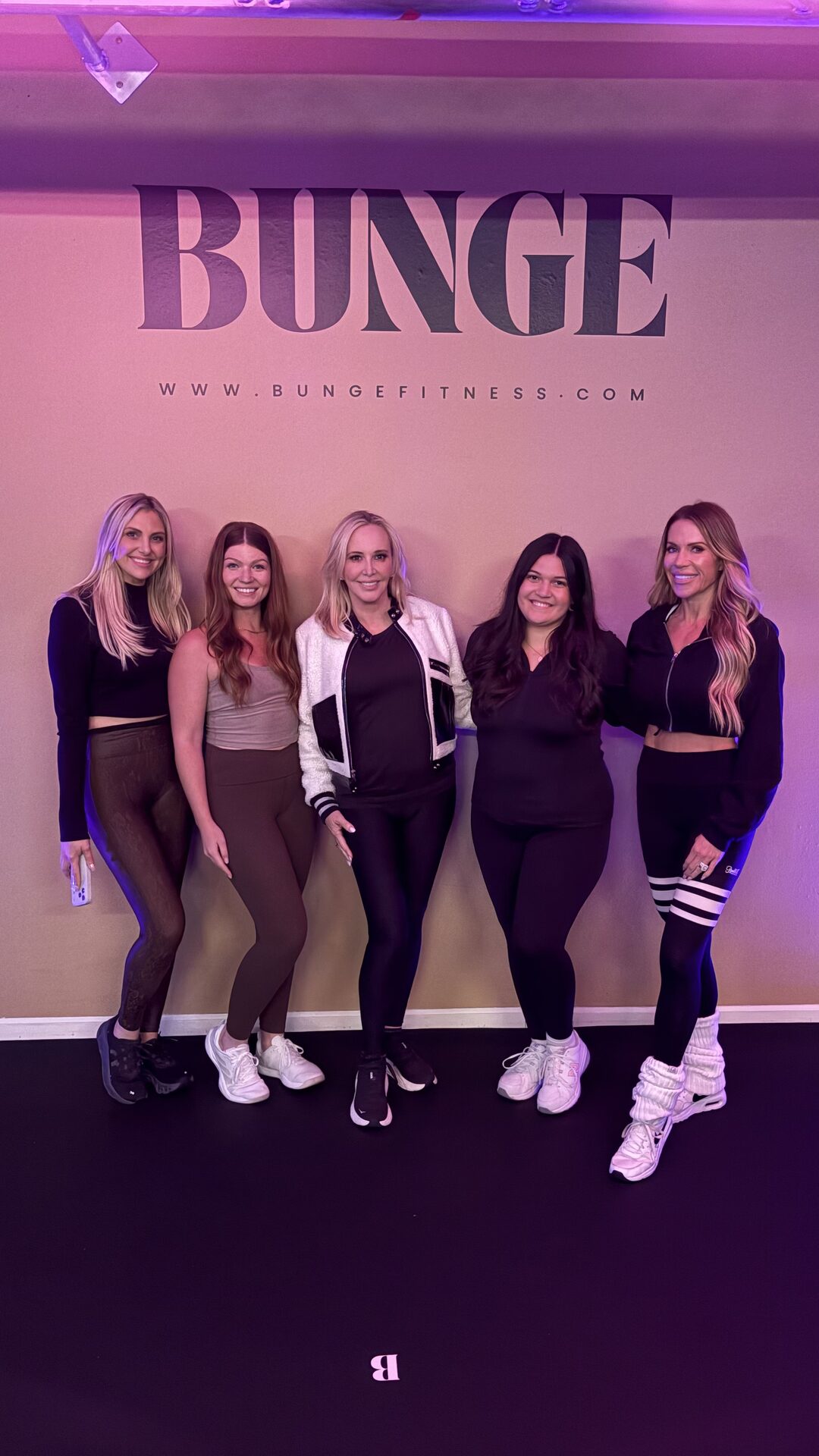 Members smiling in front of the pink-lit BUNGE logo wall after a bungee fitness class in Huntington Beach