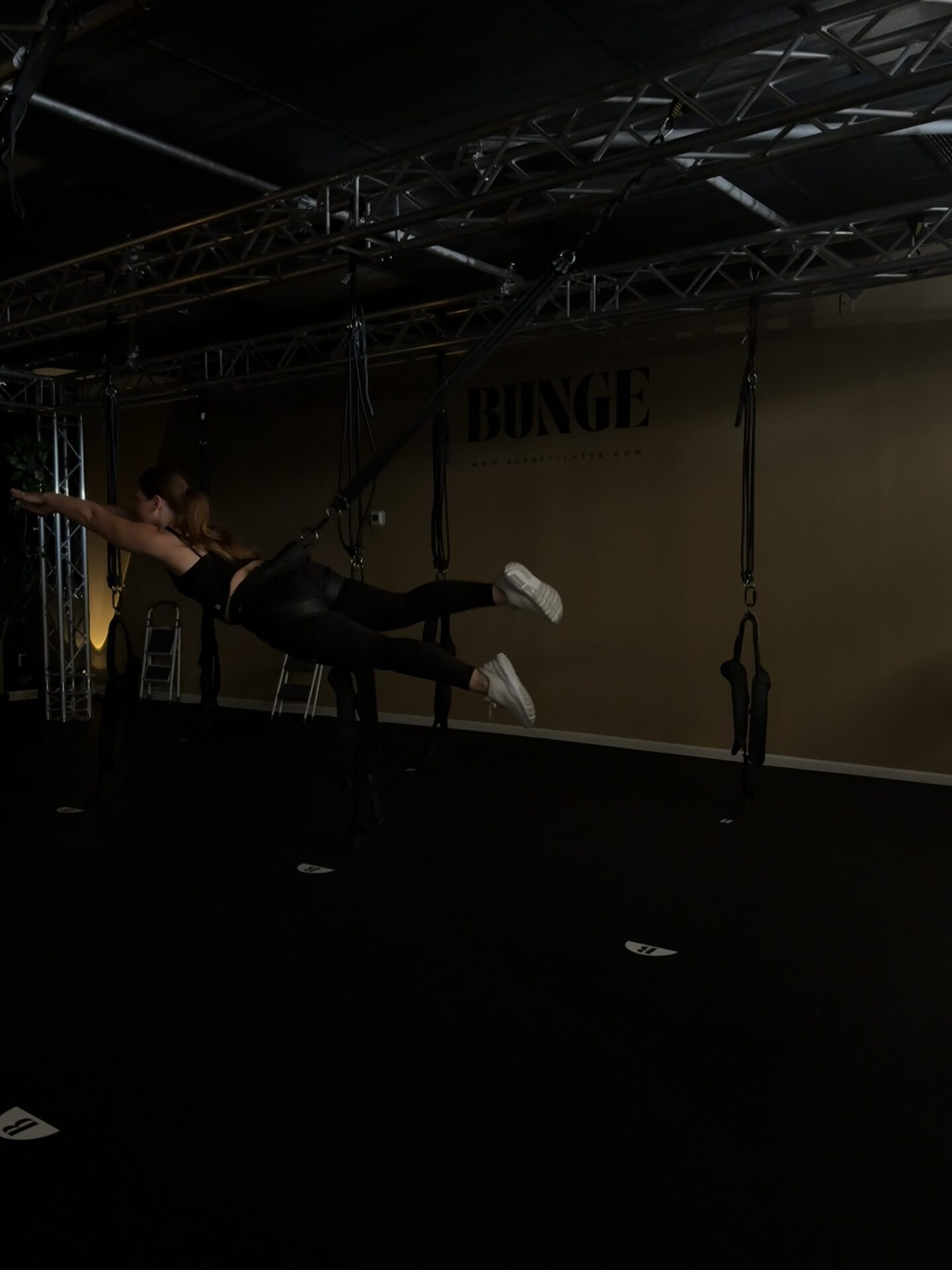 A student holding a flying arabesque pose on the bungee cord in front of the BUNGE logo wall in Huntington Beach